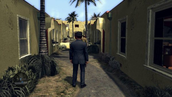 O protagonista de pé em um beco de uma vila do jogo.